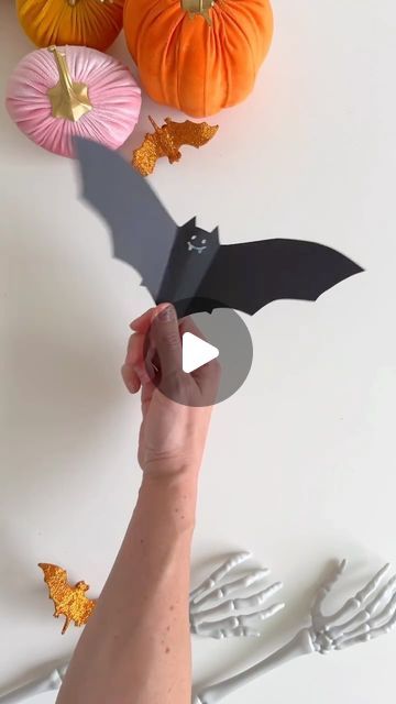 a person holding up a paper bat with pumpkins in the background