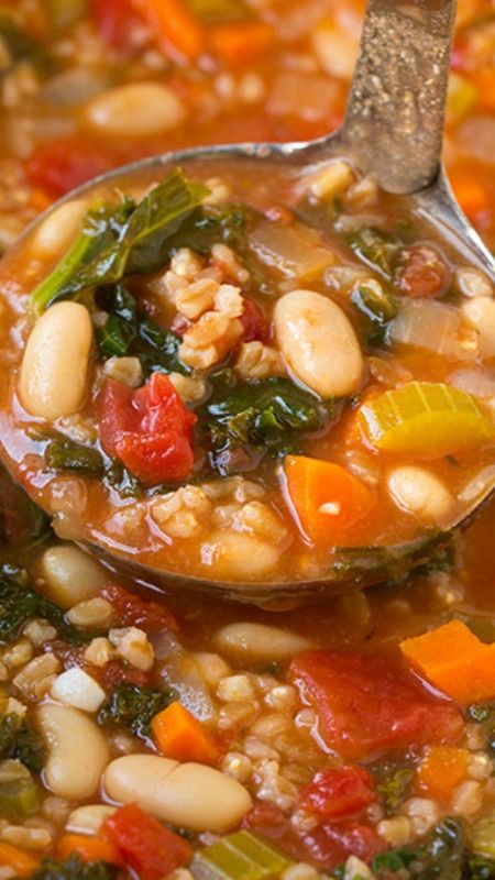 a spoon full of soup with beans and spinach in it, on top of a purple