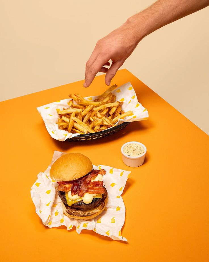 a hand reaching for a burger and french fries