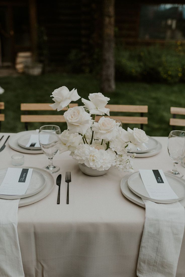 the table is set with white flowers and place settings