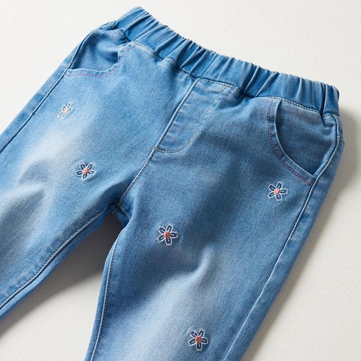 a pair of blue jeans with embroidered flowers on the bottom and side, sitting on a white surface