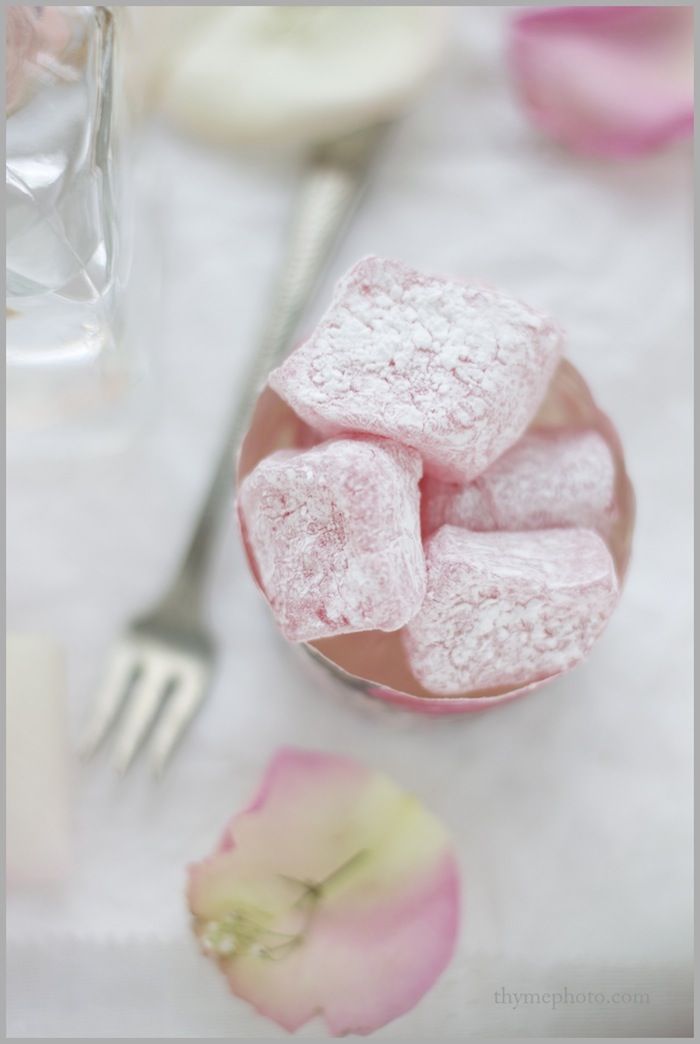 pink marshmallows are in a bowl next to a fork and flower petals