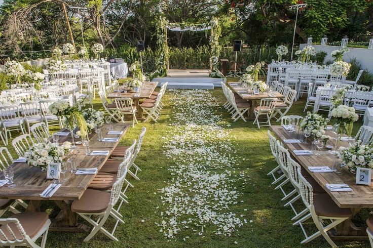 an outdoor wedding venue set up with wooden tables and white flowers on the grass, surrounded by greenery