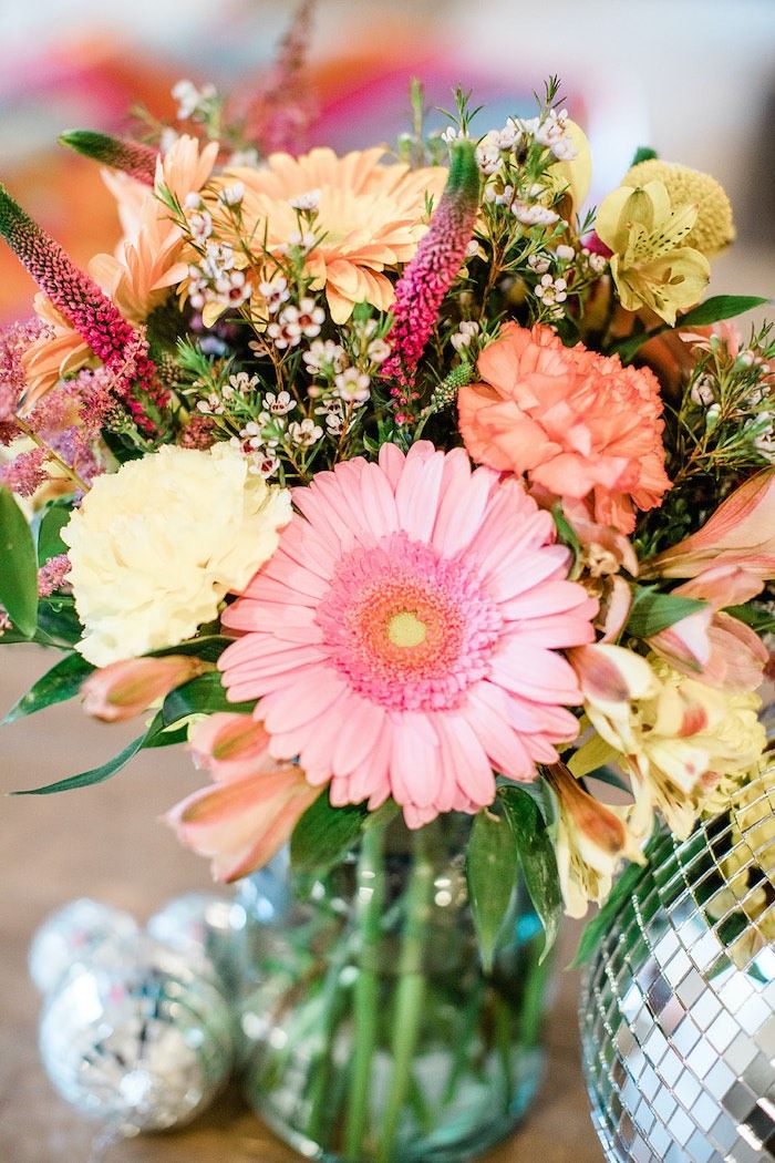 a vase filled with lots of colorful flowers on top of a table next to a disco ball