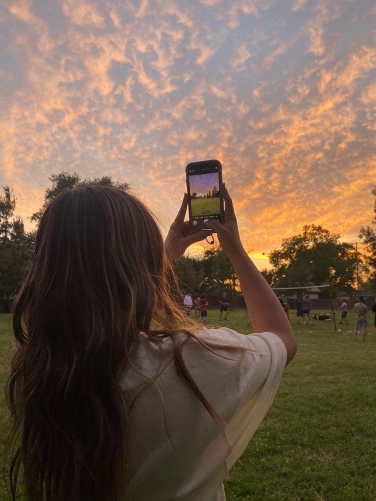 a woman is taking a photo with her cell phone in the park as the sun sets