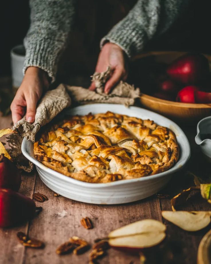 a pie with apples in the background and someone holding an apple peel over it's crust