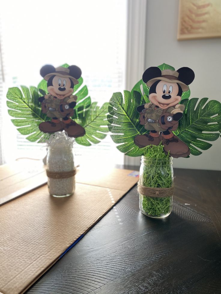 two vases filled with plants and mickey mouse cut outs on top of a table