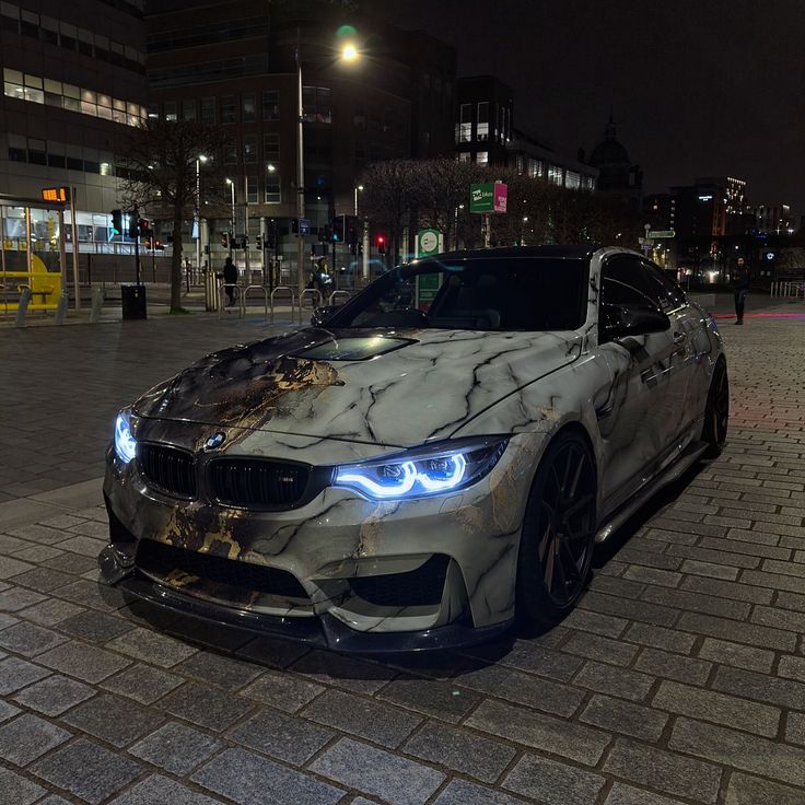 a white car parked on top of a brick road next to a tall building at night