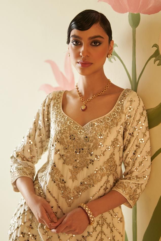 Ivory kurta with floral, gotta patti, mirror work, zari embroidery. Paired with embroidered sharara and embroidered dupatta.
Components: 3
Pattern: Embroidered
Type Of Work: Floral
Neckline: Tier drop neck
Sleeve Type: Three quarter
Fabric: Silk, Lining: Crepe
Color: Ivory
Other Details: 
Attached lining
Side slits
Back tie-up
Scallop border dupatta
Note: All the jewellery worn by the model is for styling purpose only
Occasion: Wedding - Aza Fashions Elegant Blouse Piece With Mirror Work For Wedding, Elegant Wedding Blouse Piece With Mirror Work, Elegant Wedding Blouse With Mirror Work, Elegant Off White Anarkali Set For Party, Anarkali Cream Sharara With Pearl Embroidery, Elegant Unstitched Blouse Palazzo Set For Eid, Elegant Unstitched Blouse Palazzo Set For Wedding, Festive Elegant Sharara With Unstitched Blouse, Elegant Palazzo Set With Unstitched Blouse For Reception