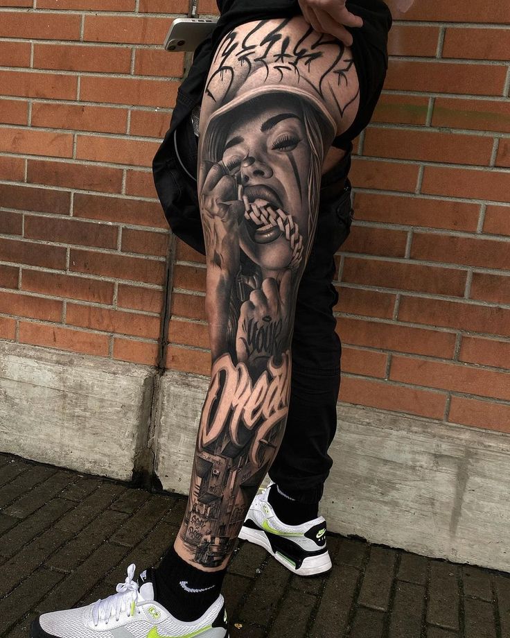 a man's leg with a black and grey tattoo design on it, next to a brick wall