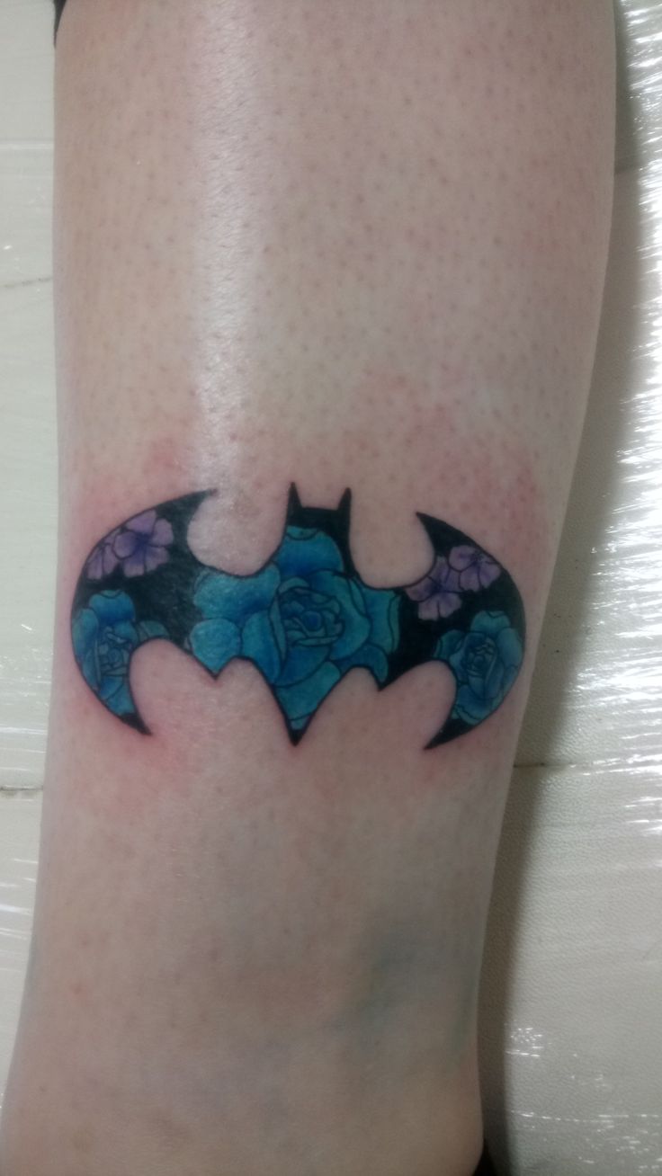 a tattoo on the leg of a woman with blue roses and a batman symbol painted on it