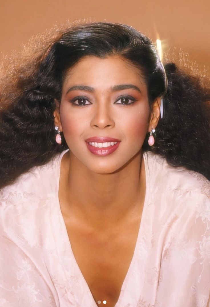 a woman with long hair wearing earrings and a white shirt is smiling at the camera