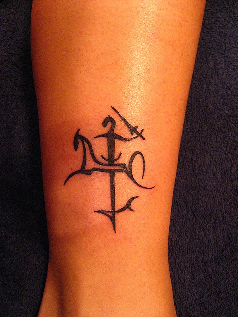 a small anchor tattoo on the foot of a woman's leg with an arrow