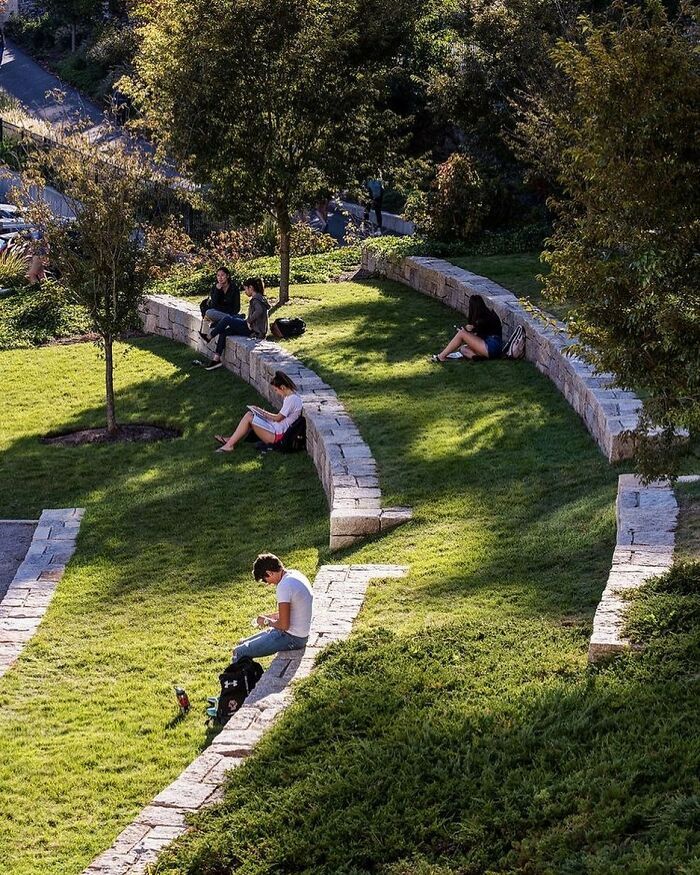 several people sitting on the grass in a park with stone walls and steps leading up to them