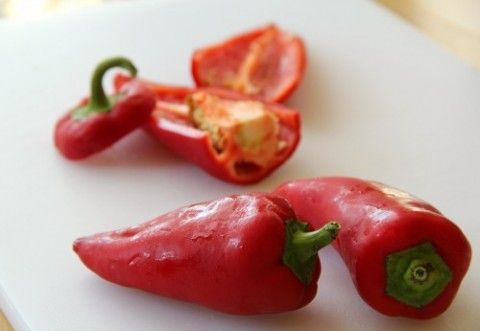 three red peppers on a white cutting board