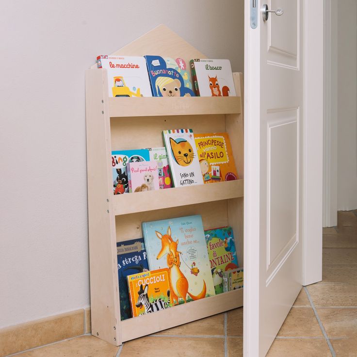 a book shelf with books on it next to a white door in a room that has tile flooring