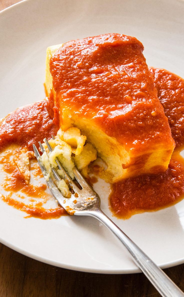 a piece of lasagna on a plate with sauce and a fork in it