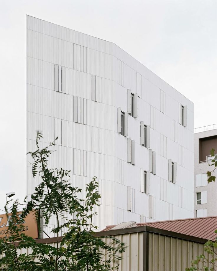 a tall white building with many windows on it's side and trees in the foreground