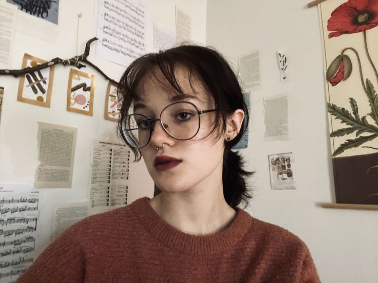 a woman wearing glasses standing in front of a wall covered with pictures and flowers on it