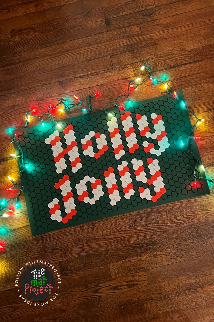 a christmas sign made out of legos with lights around it on a wooden floor