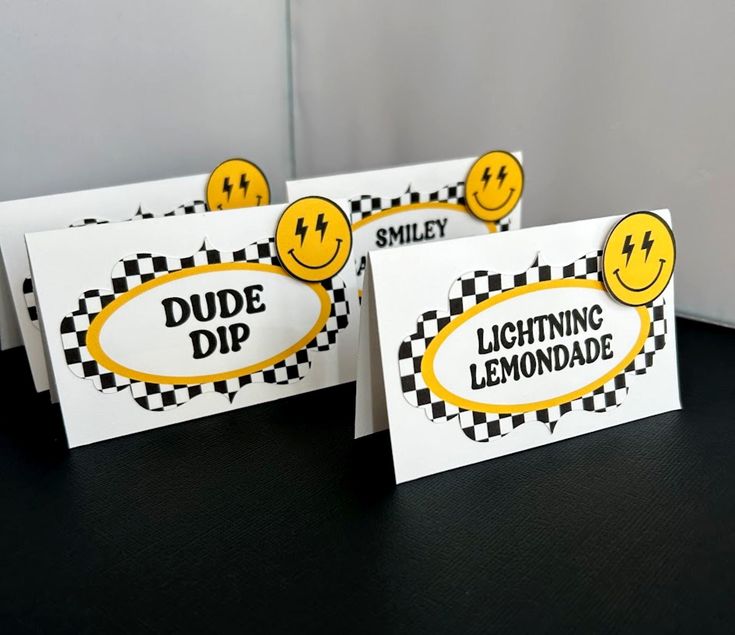 three signs with smiley faces on them are sitting on a black tablecloth covered surface