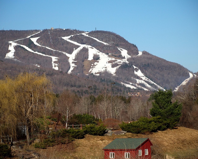 a red house sitting in the middle of a field next to a snow covered mountain