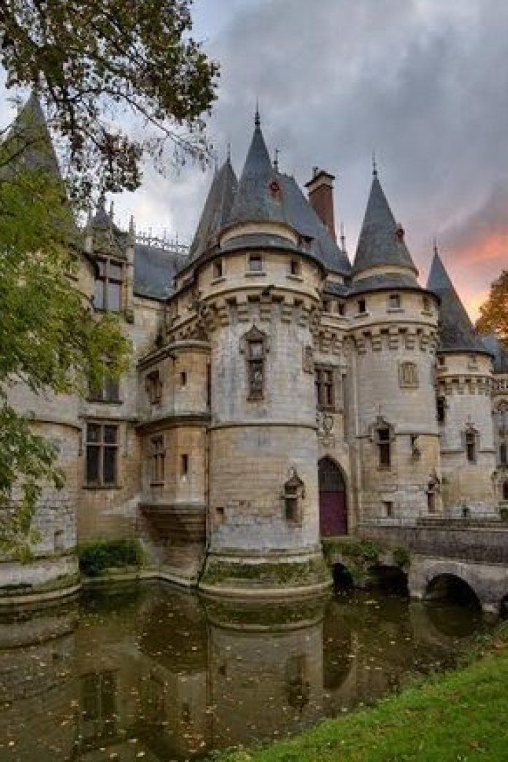 an old castle sits next to a body of water in front of a cloudy sky