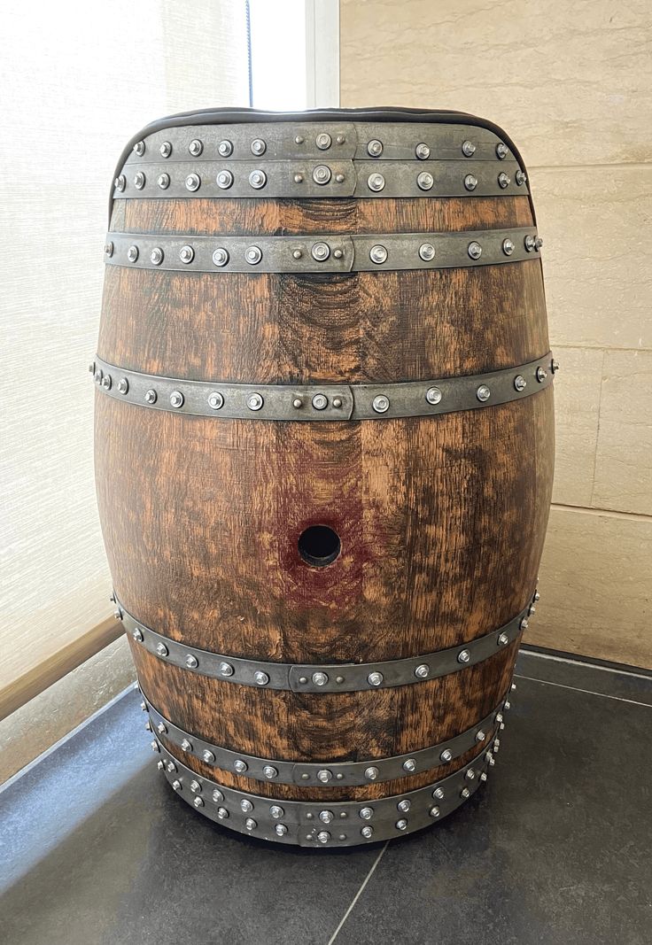 a wooden barrel with metal rivets on the bottom and sides, sitting on a tile floor