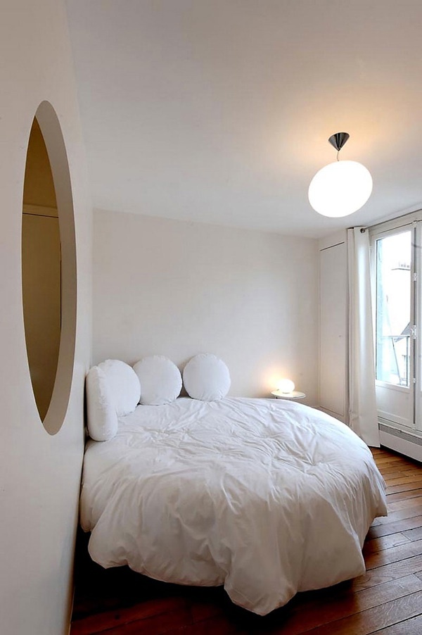 a white bed sitting next to a window in a bedroom on top of a hard wood floor