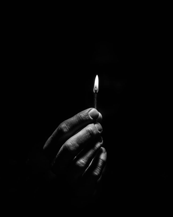 a person holding a lit candle in their hand on a dark background with only one light visible