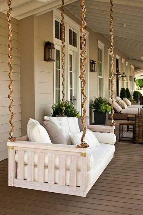 a porch swing with pillows and plants on the back deck area, hanging from two wooden posts