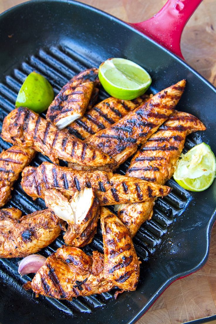 grilled chicken and limes on a grill with a red spatula next to it