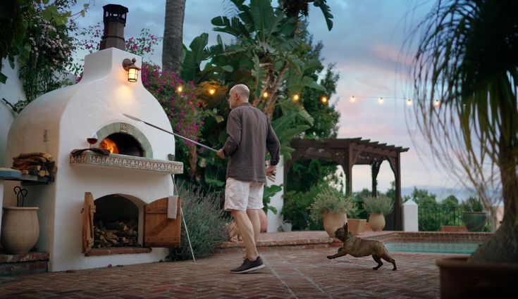 a man is walking his dog in front of an outdoor pizza oven