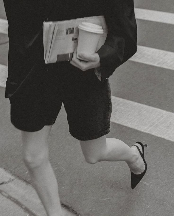 a woman walking across a street while holding a coffee cup