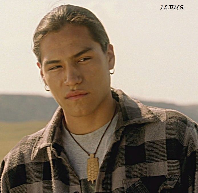 a young man wearing a necklace and looking off into the distance with mountains in the background