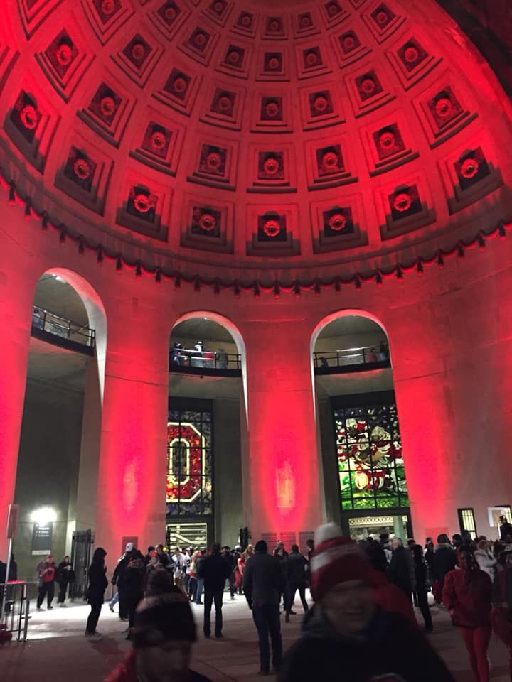 the inside of a building with red lighting and people walking around it at night time