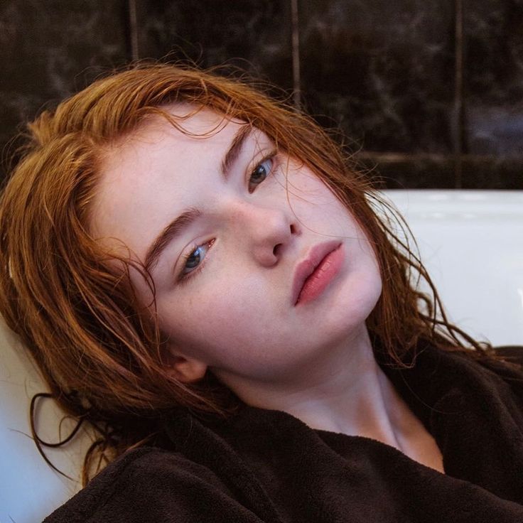 a woman with red hair laying in a bathtub