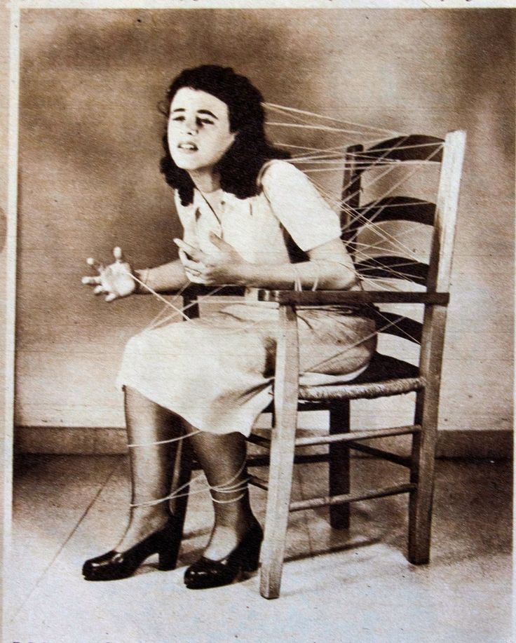 an old photo of a woman sitting in a chair with yarn on her legs and feet