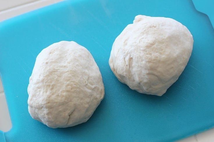 two uncooked balls of dough on a blue cutting board