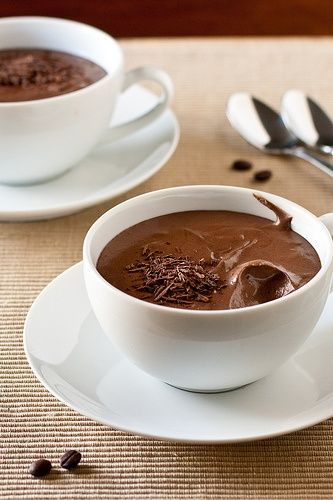 two white bowls filled with chocolate pudding on top of a table next to spoons