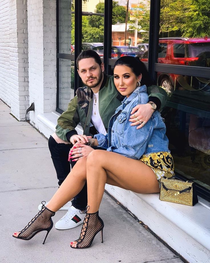 a man sitting next to a woman on the side of a building with her legs crossed