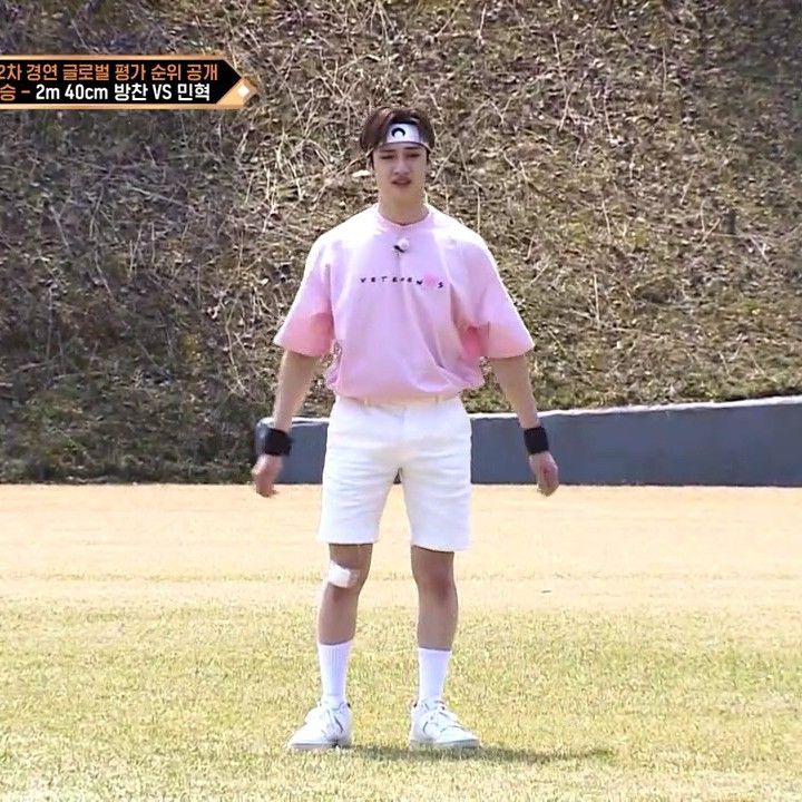 a man in pink shirt and white shorts playing frisbee on grass with bushes behind him