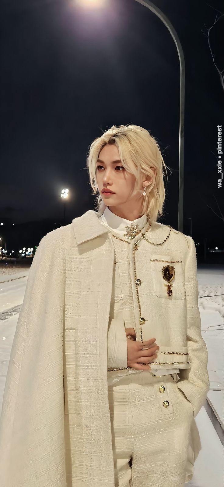 a woman with blonde hair wearing a white coat and pants standing in the snow at night