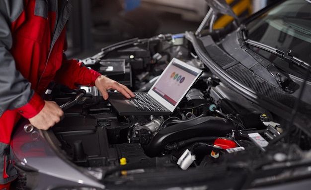 a man working on his laptop in front of a car engine