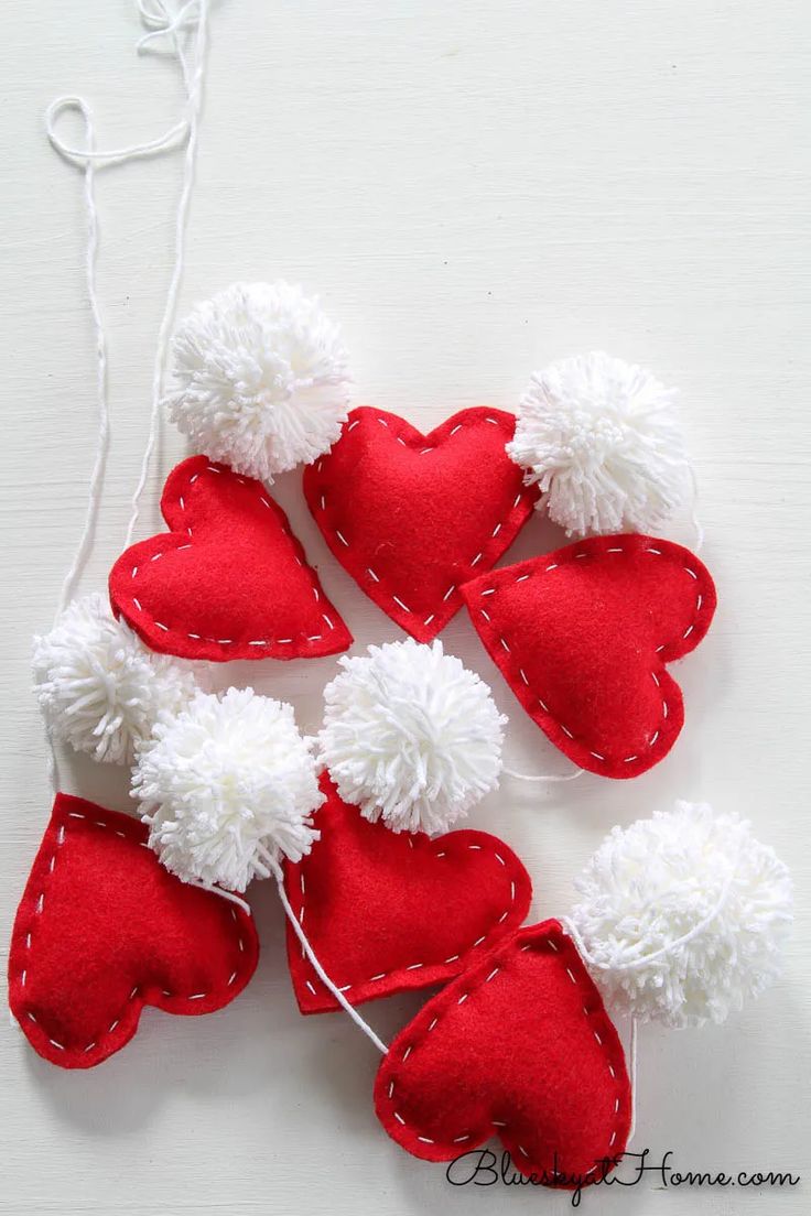 four red and white felt hearts hanging from a string on a white table with strings