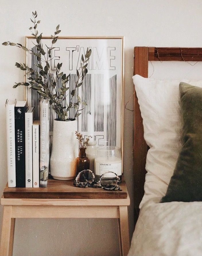 a bed with books and plants on top of it next to a framed poster that says let time go by