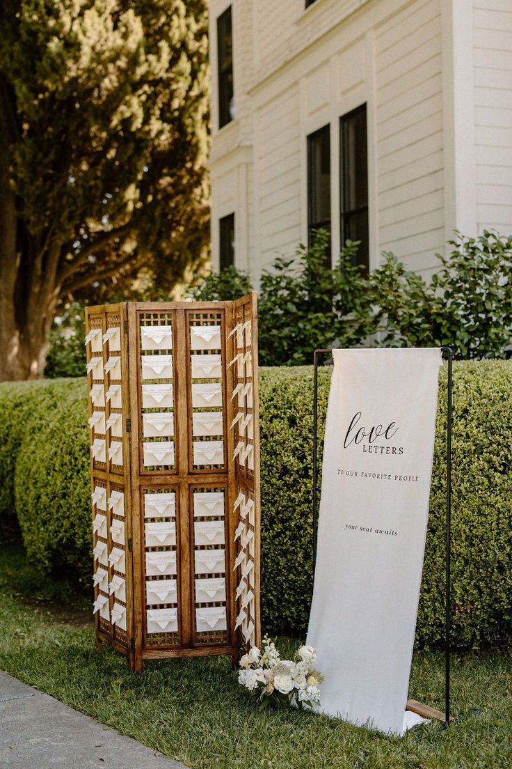 an outdoor ceremony setup with a wooden screen and white flowers on the grass next to it