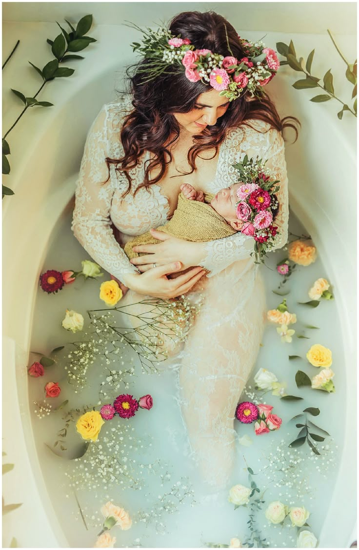 a woman is sitting in a bathtub with flowers around her and holding a baby