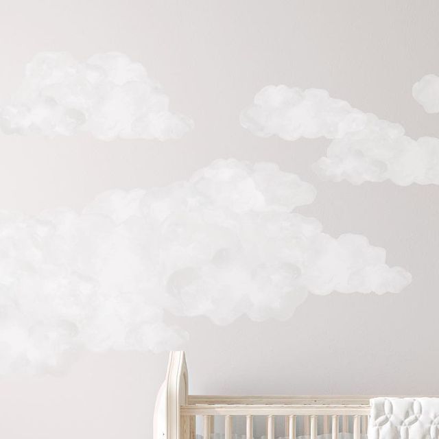 a baby crib in front of a white wall with clouds painted on it