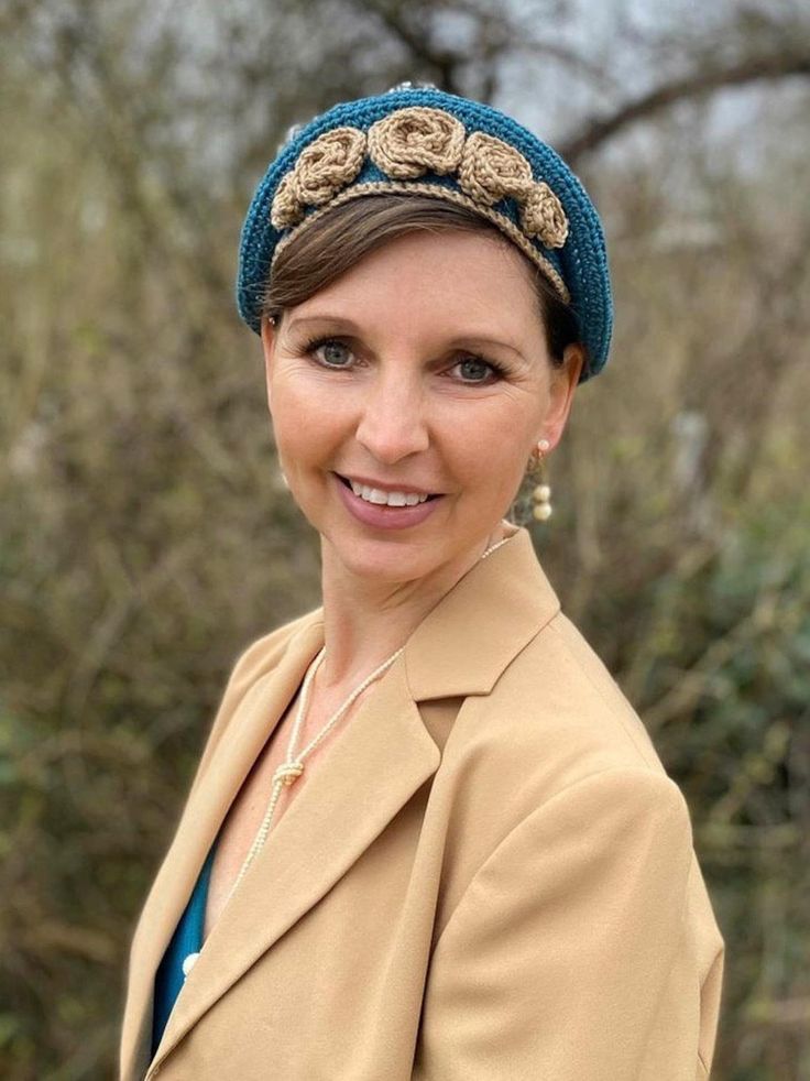 a woman wearing a blue hat and coat posing for a photo with trees in the background